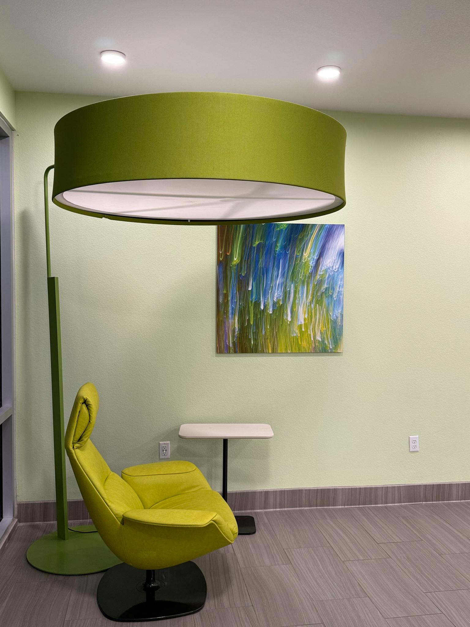 A sleek modern interior featuring a green lamp and chair against a soft pastel backdrop.